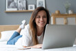 © opolja - Portrait of a beautiful smiling young woman using laptop in bed at home.