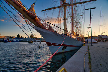 Wall Mural - Big historic sailing ship in the port. Yachts and boats at sea against the backdrop of the setting sun. Sailboat travel concept.