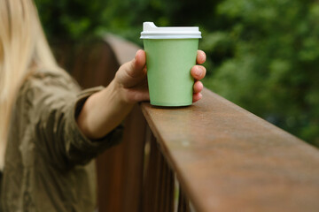 Green paper cup with coffee in woman hand. Time for drink coffee in city. Coffee to go. Enjoy moment, take a break. Disposable paper cup closeup. Delicious hot beverage. Blank space for text, mockup