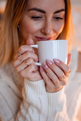  Portrait of a pretty blonde in a cozy home sweater with a Cup of tea or coffee in her hands with rings and a beautiful manicure.