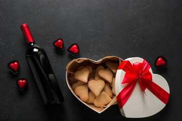 Bottle of red wine and heart cookies in gift on black. Valentine's Day Greeting card. View from above. Space for text.