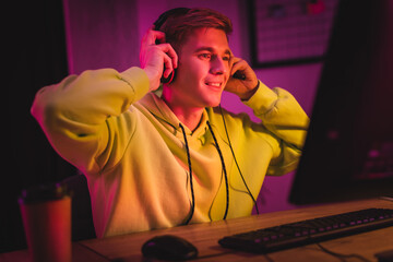 Smiling gamer wearing headset near computer and coffee to go on blurred foreground