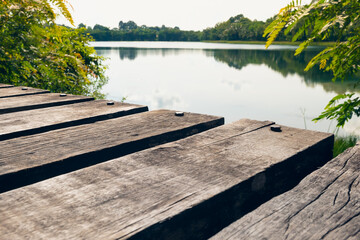 Close up view of rustic wooden bridge above the pond against reflection of sky and trees on calm water background.