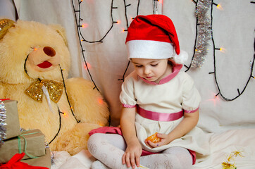  Funny child in Santa Claus hat on a Christmas background.Congratulatory New Year card with a place for an inscription.Happy child.New Year. Happy child with a tangerine in his hands for the New Year.