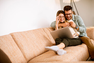 young couple using laptop together while sitting on sofa at home