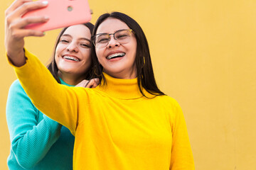 two pretty young smiling hispanic women in blue and yellow sweaters with braces on their teeth taking a selfie. friendship concept.