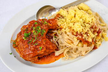 Wall Mural - Stewed rooster in tomato sauce, served with homemade pasta and cheese. Traditional Greek dish