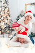 © Serenkonata - Happy family under Christmas tree. baby boy in Santa Claus hat with gifts under Christmas tree with many gift boxes presents