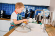 a boy in an apron washes dishes in the kitchen at home.
