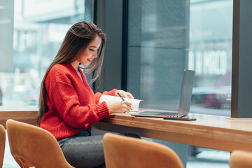 young smiling beautiful Asian freelancer woman holding smartphone with laptop in cafe, writing on mobile phone, business women working with laptop computer and communicating online via smartphone