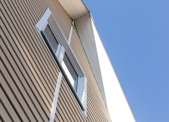 The facade of the new house clad with siding, with windows, against the blue sky.