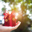 Hand hold gift box to someone on green bokeh nature. Celebration holiday.