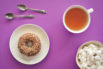 Canvas Print - Tea break concept. Chocolate donut, tea cup, sugar cubes, tea spoons on violet background.