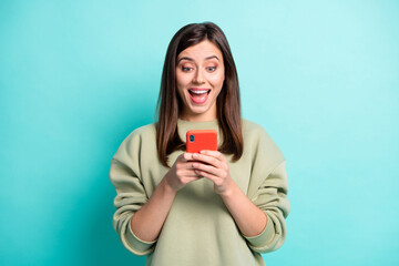 Sticker - Photo portrait of excited girl with open mouth holding phone in two hands isolated on vivid teal colored background