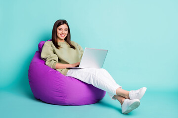 Poster - Photo portrait full body view of girl working on laptop sitting in purple beanbag armchair isolated on vivid teal colored background