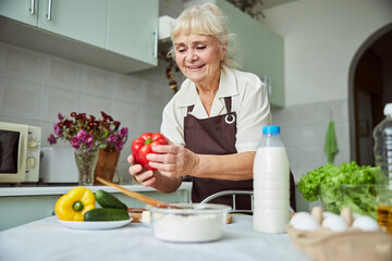 Wall Mural - Joyful old woman cooking dinner at home