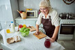 © Viacheslav Yakobchuk - Cheerful old woman cooking dinner and using laptop in kitchen