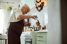 Joyful Senior Woman In Apron Cooking Dinner In Kitchen
