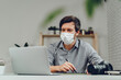 © fotofabrika - Man working on laptop at home and wearing medical mask