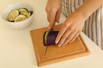 Woman chopped eggplant on wooden board on white table