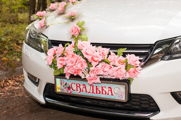 Beautiful white car for the bride and groom, decorated with pink flowers with the inscription Wedding