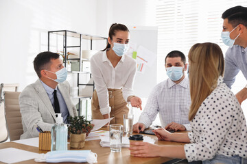 Wall Mural - Group of coworkers with protective masks in office. Business meeting during COVID-19 pandemic