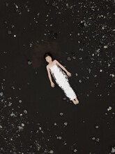 Girl Wrapped In Silver Foil Laying On Ground Of Black Lava Rocks In Iceland Seen From Above
