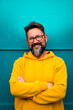 © simona - Portrait of cheerful adult handsome man smile with yellow sweater clothes and blue wall in background - happy people and copy space - beard 50 years old male with black eye glasses