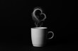 Steaming coffee cup on black background. White сoffee cup with steam. Smoke from hot coffee. Front view, copy space