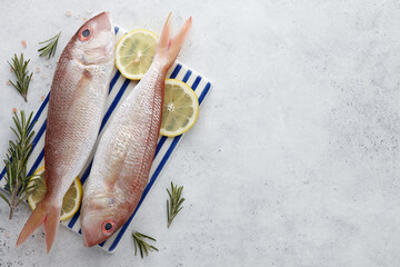 Poster - Raw red mullet fish with lemons and herbs on white stone background, copy space