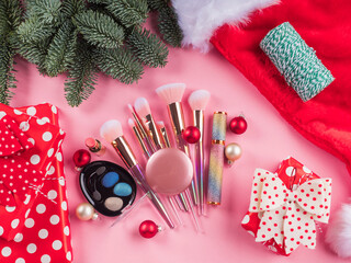 Wall Mural - Christmas spruce branches, santa cap and presents with shiny make up tools, products on pink background. Festive beauty gift concept