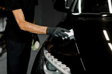 Protection the car body from scratches, chips and damage. Cropped close up shot of process of applying a nano-ceramic coating on the car's hood by a male worker with a sponge and special composition