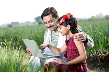 Farmer with daughter using laptop on agriculture field