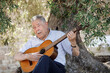 © alex.pin - Uomo ottantenne suono malinconico  una melodia seduto all'ombra di un vecchio ulivo in campagna