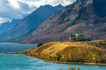 Middle Waterton Lake lakeshore in autumn foliage season sunny day morning. Blue sky, white clouds over mountains in the background. Landmarks in Waterton Lakes National Park, Alberta, Canada.