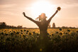 © Francisco Carrodeguas/ADDICTIVE STOCK - Back view silhouette of unrecognizable female in hat standing with arms raised among blooming sunflowers and enjoying freedom in summer evening in field