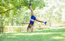 Upside Down View Of Flexible Ethnic Female Athlete In Sportswear Performing Cartwheel On Green Lawn In Park During Training