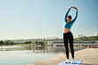 © Sergey Mironov/ADDICTIVE STOCK - Full body of young fit female in sportswear and sunglasses stretching arms while warming up during fitness workout on wooden pier near river