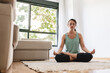© Sergio Victor Vega/ADDICTIVE STOCK - Peaceful female in sportswear practicing yoga in lotus pose while sitting on carpet in living room