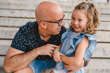 Smiling Male Embracing Adorable Little Girl While Sitting On Stone Stairs During City Stroll