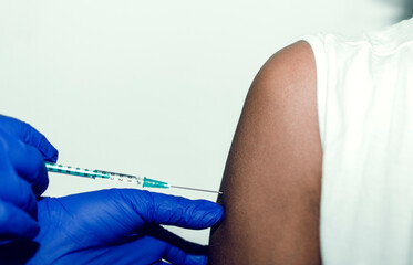 Closeup of a doctor wearing blue gloves injecting a syringe in a black woman's arm.  Covid-19 vaccine. Selective focus on the arm.