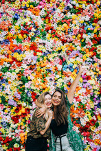 Cheerful Female Friends Embracing While Standing Against Colorful Flowers