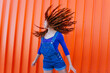 © VISTA by Westend61 - Playful woman tossing hair while standing against orange wall