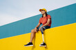 © VISTA by Westend61 - Young man smiling while sitting on wall against clear sky