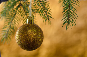 Golden ball on a Christmas tree branch, on a gold background.