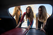 © David Prado/Stocksy - Happy females putting bags in trunk of car
