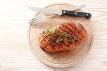 Crispy Grilled Duck Breast With Rosemary Garnish On A Wooden Cutting Board With Fork And Knife, High Angle View From Above