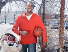 African Man Carrying Baby In Carrier And Holding Basketball