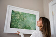 © JGI/Jamie Grill/Blend Images - Mixed Race woman hanging picture frame on wall