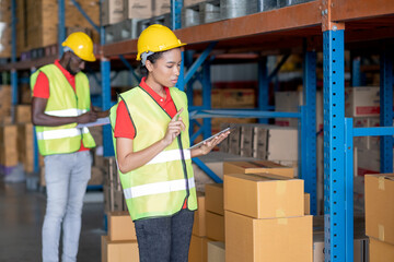 Wall Mural - African American warehouse worker use tablet to check product in stock with her co-worker man work in background. Concept of good management system to support working with industrial business.